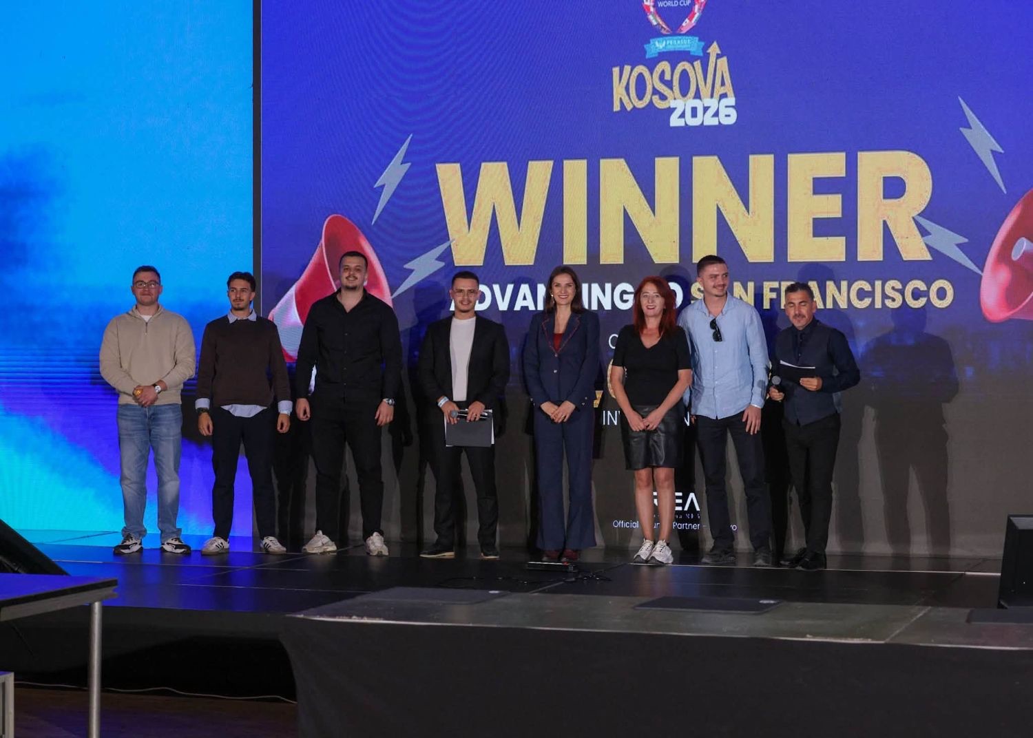 The WiseUnit team on stage with the hosts in front of the screen announcing the Startup World Cup Kosova 2026 winner, advancing to San Francisco.